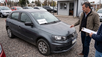 Un hombre mira un automóvil gris usado con un cartel de 15.861.000 pesos en el parabrisas junto a otra persona con una carpeta de papeles.
