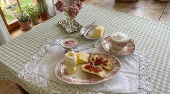 Mesa con mantel a cuadros verde y blanco, un plato con huevo, queso y tostadas, un tazón de yogur, una taza de café, mantequilla y flores.