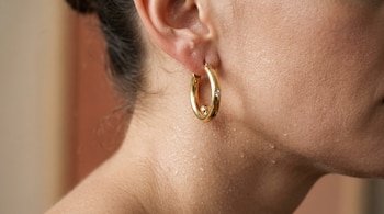 Lóbulo de una oreja con un aro de oro y pequeñas gotas de agua o sudor sobre la piel del cuello.