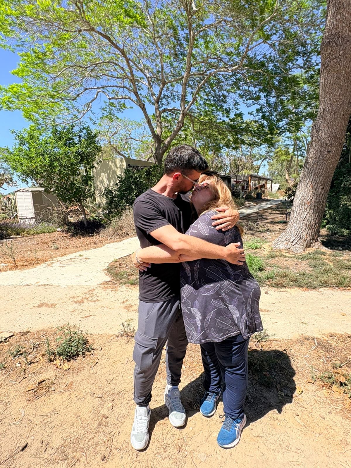 Ariel Cunio y su madre Silvia Cunio expresan su amor con un abrazo y un breve beso, el martes 2 de junio, en el kibutz Nir Oz, donde fue secuestrado él y su hermano David el 7 de octubre de 2023. Detrás las ruinas de sus casas. (Infobae)