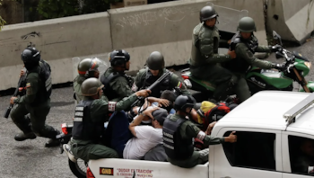 Agentes de seguridad con cascos y chalecos sujetan a personas en la parte trasera de una camioneta blanca junto a motocicletas