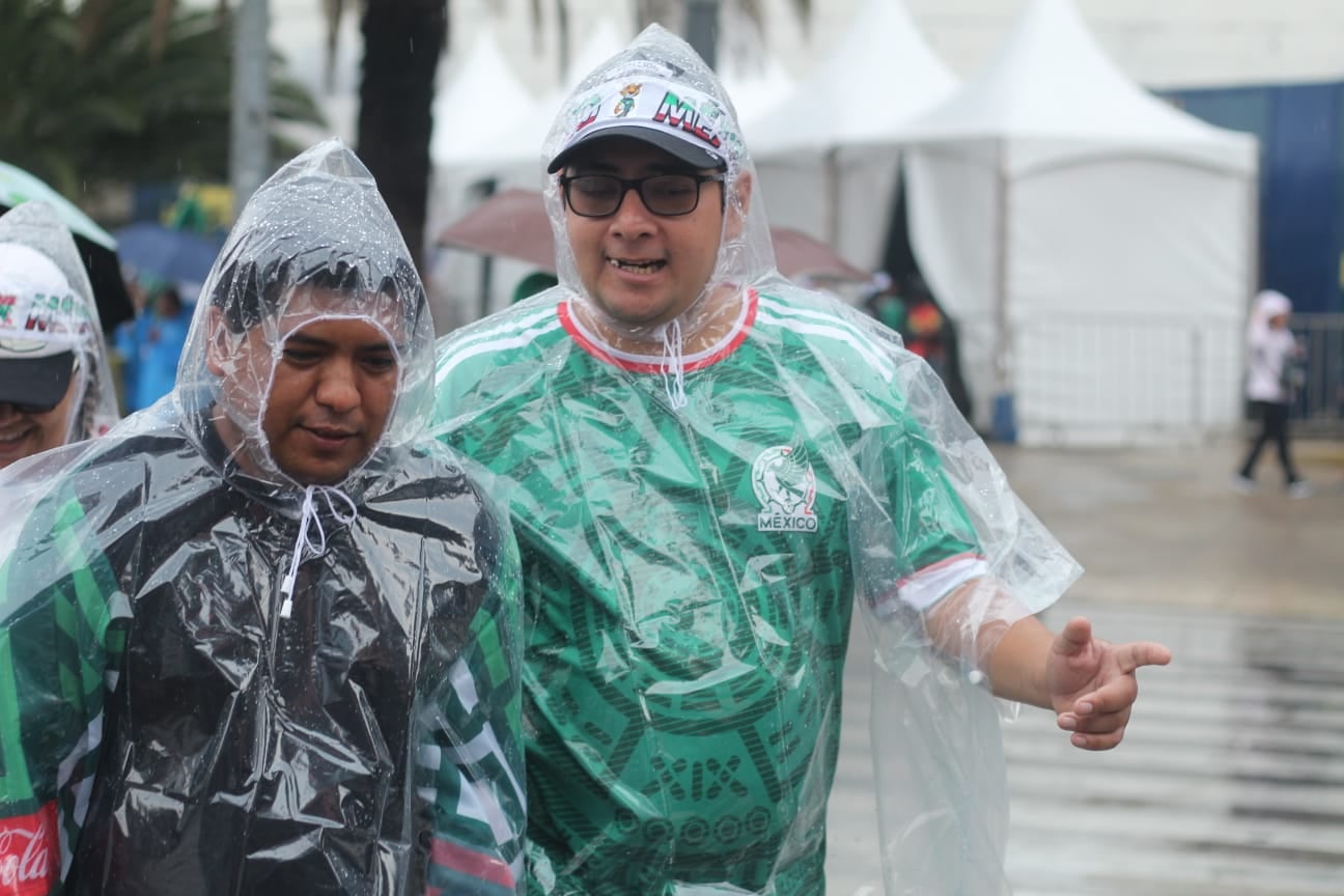 Dos aficionados mexicanos, protegidos con ponchos transparentes, asisten a la despedida de la Selección Nacional bajo la lluvia. (@OVIALCDMX)