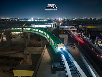 Tren Metrorrey verde y blanco con luces encendidas en vía elevada de concreto de noche, con obras de construcción abajo y luces de la ciudad de fondo