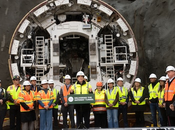 Un grupo de personas con cascos y chalecos reflectantes posa frente a una gran tuneladora redonda en una obra subterránea
