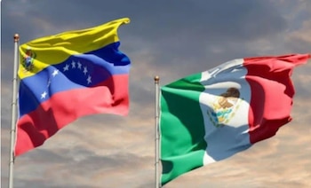 Dos banderas, una de Venezuela y otra de México, ondean en mástiles individuales bajo un cielo nublado