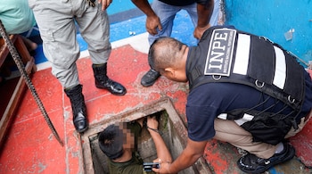 Un agente con chaleco del Instituto Nacional Penitenciario observa a una persona dentro de un pozo rectangular en el suelo.