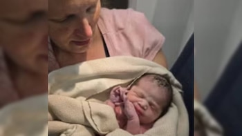 Primer plano de una mujer de piel clara con una camisa rosa sosteniendo a un recién nacido envuelto en una manta de color claro