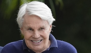 Primer plano de Mike Jeffries, un hombre de cabello blanco con una prenda azul oscuro que sonríe sobre un fondo verde