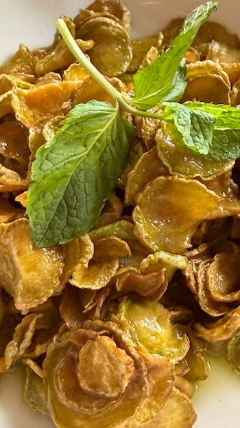 Primer plano de un plato con rodajas doradas y translúcidas, cubiertas con almíbar, y una rama de menta verde en la parte superior