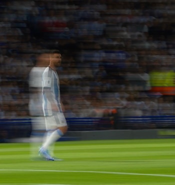 Hombre con camiseta de fútbol de Argentina con rayas celestes y blancas y el número diez, en movimiento borroso, sobre un fondo oscuro con tonos rojos