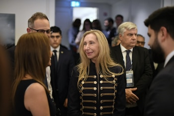 Karina Milei sonríe vestida con una chaqueta oscura con botones dorados mientras conversa con personas de traje en un pasillo