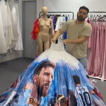 Una falda de tela circular extendida en el piso con retratos de Lionel Messi, en una habitación con percheros de ropa y un sofá