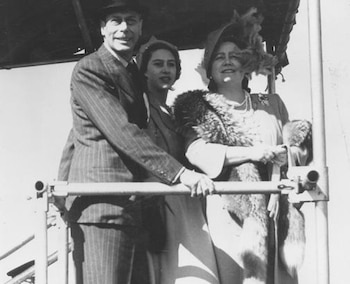 Fotografía en blanco y negro de tres personas con vestimenta formal y sombreros, paradas detrás de una baranda metálica