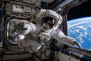 Un astronauta con traje espacial blanco y bandera de Estados Unidos flota en el interior de una estación espacial con la Tierra visible a través de un ventanal