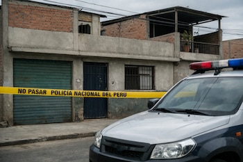 Fachada de vivienda urbana popular peruana con cinta policial amarilla 'NO PASAR POLICÍA NACIONAL DEL PERÚ' y el frente de un patrullero estacionado.
