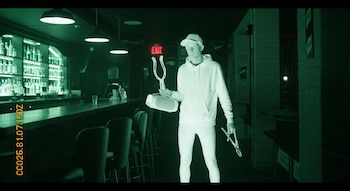 Hombre con gorra, sudadera, altavoz y tenazas metálicas en un bar con luz infrarroja y una marca de tiempo en la esquina inferior izquierda.