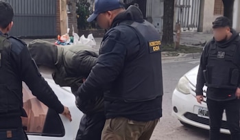 Agentes de la DDI con chalecos antibalas sostienen a un hombre encapuchado junto a un automóvil blanco en la vía pública