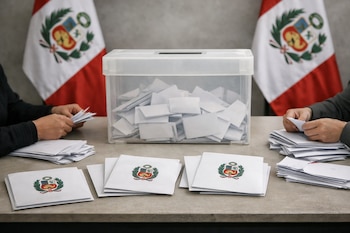 Manos cuentan votos en sobres sobre una mesa de escrutinio, con una urna transparente llena de boletas y banderas de Perú al fondo.