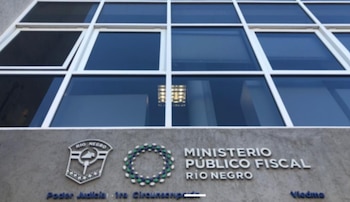 Fachada de un edificio con grandes ventanas de cristal reflectante y un letrero que dice Ministerio Público Fiscal Río Negro, junto a dos escudos