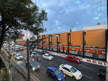 Tren del Metro CDMX en vía elevada con nueva fachada de paneles naranjas sobre una avenida con múltiples coches y un cielo nublado al atardecer