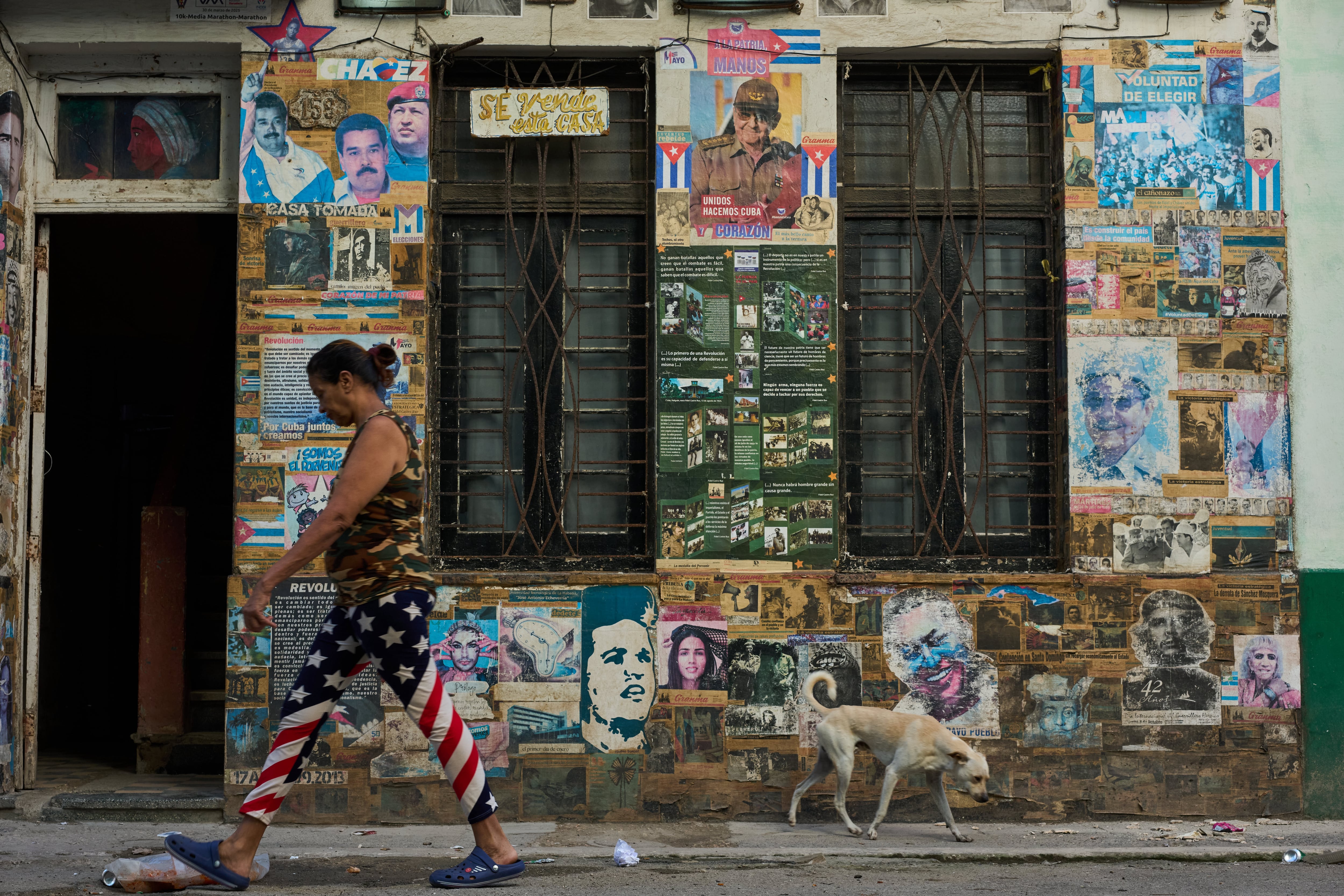 Una mujer que lleva unos pantalones con motivos de la bandera estadounidense pasa junto a un edificio que alberga una instalación artística sobre la Revolución Cubana, en la que se exhiben fotografías del expresidente cubano Raúl Castro y del expresidente venezolano Nicolás Maduro, en La Habana, Cuba, el martes 19 de mayo de 2026
(AP Foto/Ramón Espinosa)