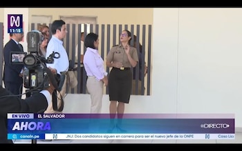 Dos mujeres sentadas frente a una mesa con copas de agua y letreros de identificación, con una bandera de Perú al fondo