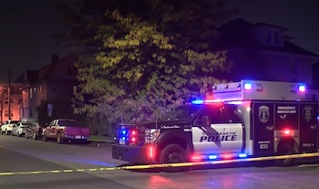 Un vehículo policial con luces de emergencia permanece detrás de una cinta de seguridad en una calle residencial durante la noche