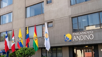 Fachada de un edificio gris con el letrero Parlamento Andino y banderas de Chile, Perú, Ecuador, Colombia, Bolivia y la institución.