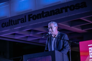 Un hombre con anteojos y saco habla ante un micrófono en un atril, debajo de un cartel con el texto Cultural Fontanarrosa