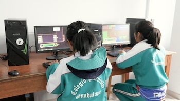 Dos estudiantes con uniforme escolar turquesa del Colegio Particular Guadalupe juegan un videojuego educativo de matemáticas en computadoras de escritorio en un aula