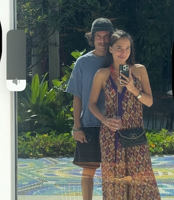 Majo Aguilar y Diego Rangel posan sonrientes para una selfie de espejo. Ella lleva un vestido estampado y él una camiseta azul y gorro, con vegetación de fondo