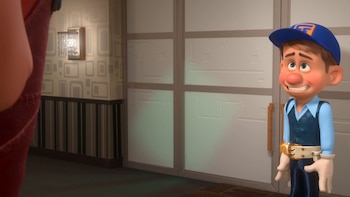Personaje animado Fix-It Felix Jr. con gorra azul, camisa celeste, chaleco y guantes blancos, sonríe forzadamente y mira hacia arriba en una habitación con papel pintado geométrico