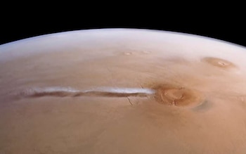 Vista de la superficie del planeta Marte con una delgada línea de nube blanca que surge de la caldera redonda de un volcán