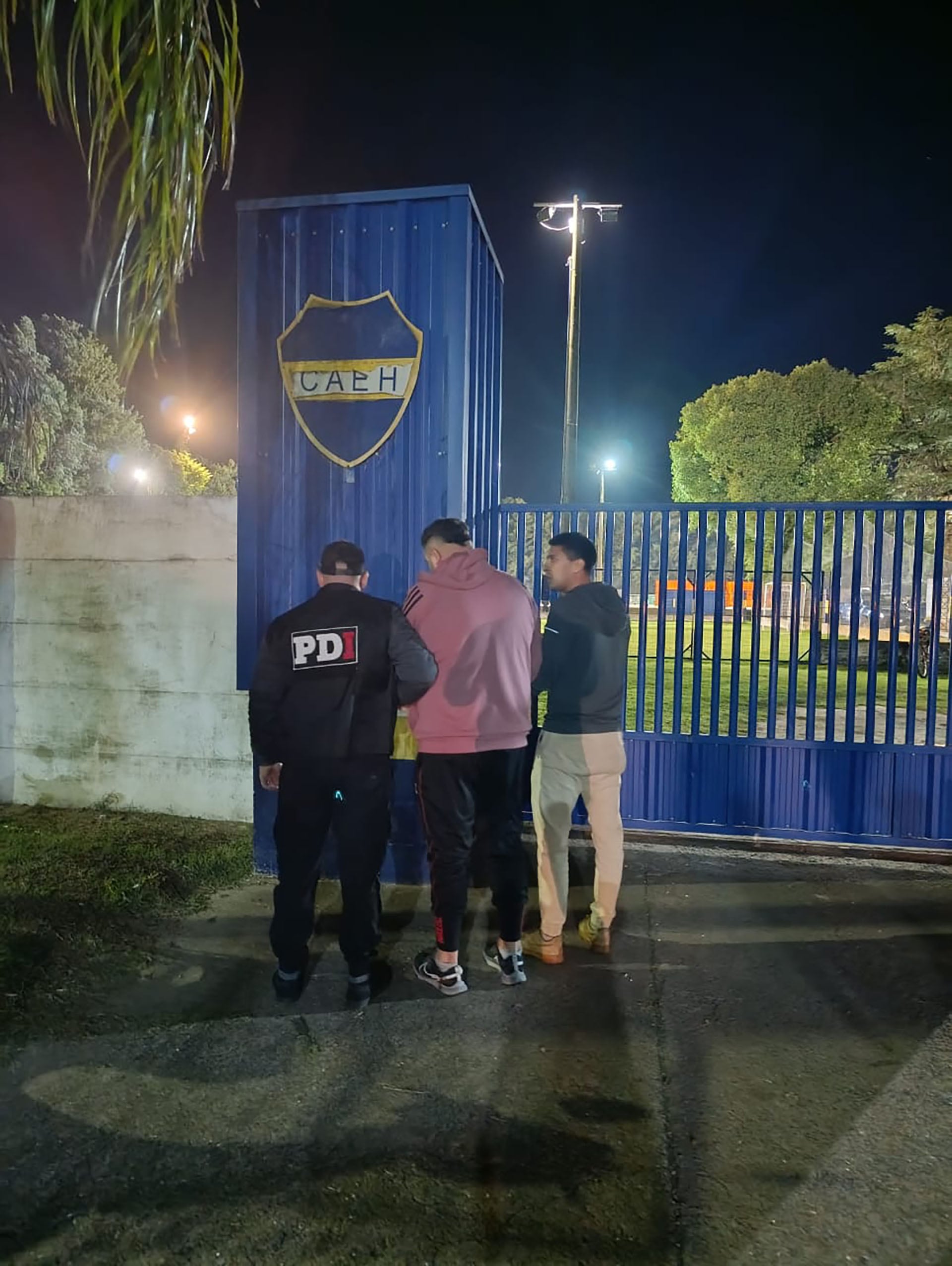 Agentes de seguridad detienen a 'Gordo' Axel, el narcotraficante de Rosario que se ocultaba como preparador físico, frente a una instalación deportiva por la noche.