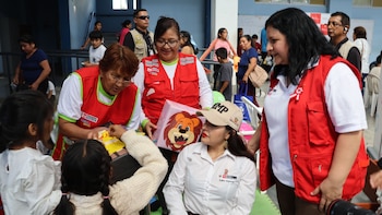 Varias personas adultas y dos niñas en un evento. Tres mujeres usan chalecos rojos. Una mujer con gorra beige lleva un gafete de identificación