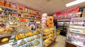 Interior de tienda con estantes llenos de productos, vitrinas de panadería con panes y pasteles, y pilas de cajas de panettone. Un letrero rojo dice 'Mi Vieja Bakery'