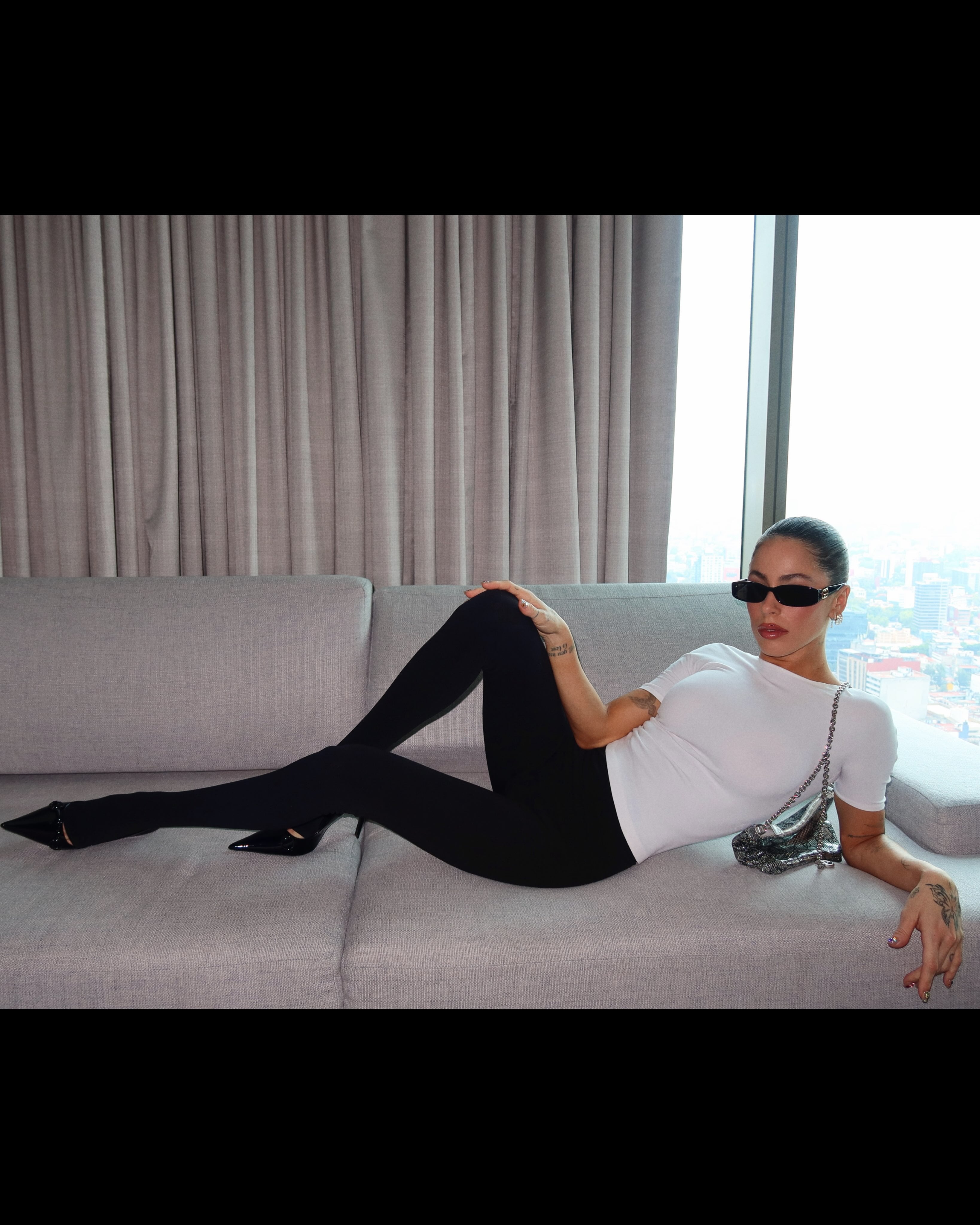Tini Stoessel, recostada en un sillón gris, con la cartera metálica en la mano
