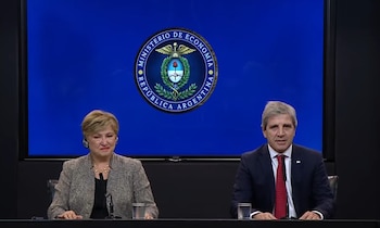 Kristalina Georgieva y Luis Caputo sentados en una mesa, frente a un panel azul con el logo del Ministerio de Economía de la República Argentina, dos vasos de agua