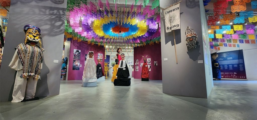 Una sala del Museo Nacional de Culturas Populares alberga una muestra de máscaras, trajes tradicionales y papel picado colorido suspendido del techo. (Sistema de Información Cultural/Gob de México)