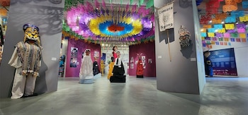 Una sala de museo exhibe figuras con máscaras y vestimentas tradicionales debajo de tiras de papel picado de varios colores
