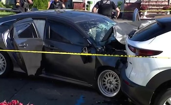 Un automóvil oscuro con el parabrisas roto y daños frontales junto a un vehículo blanco, acordonados con cinta amarilla de la policía