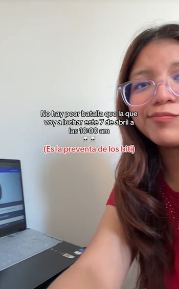 Vista parcial de una mujer joven con gafas y cabello largo que mira la cámara. A su izquierda, se ve un portátil abierto con pantalla oscura