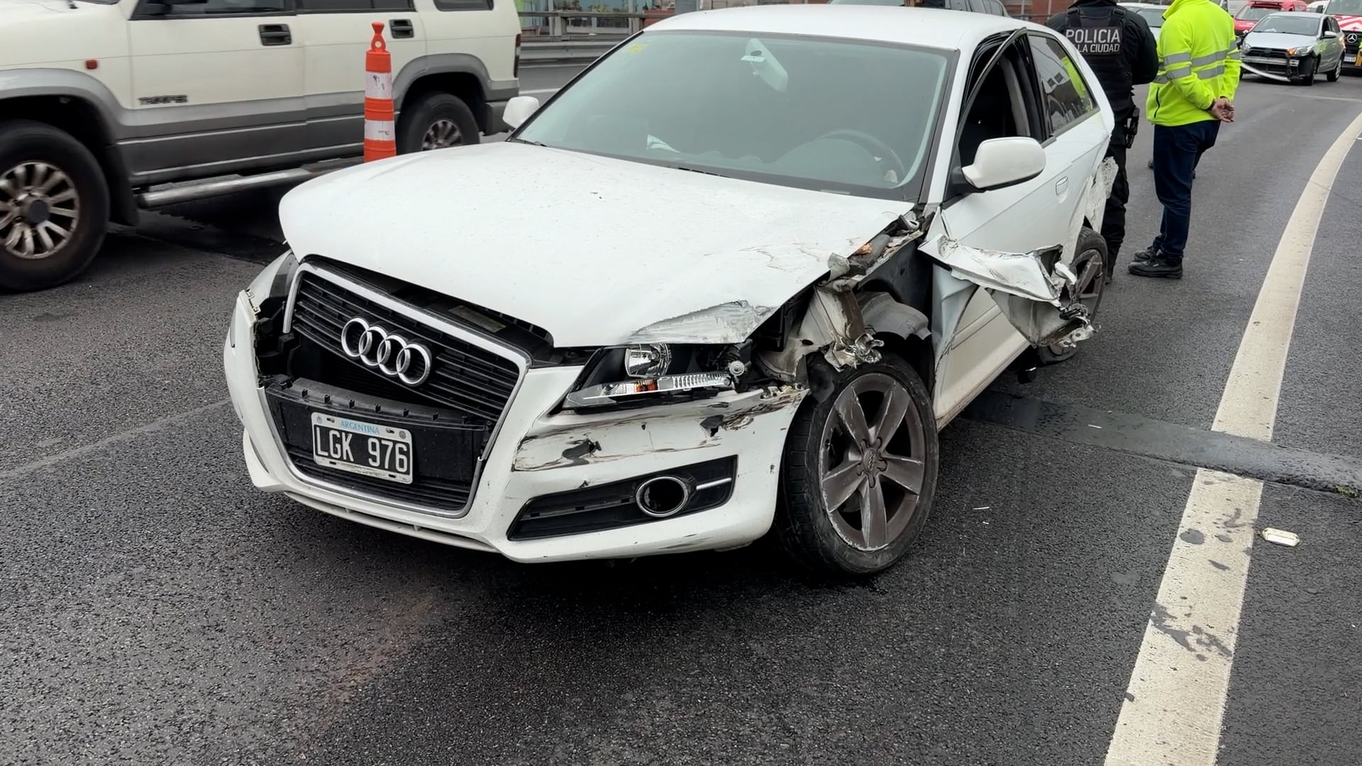Un automóvil Audi blanco con severos daños frontales permanece en el lugar de un choque múltiple en Retiro, con personal policial y otros vehículos presentes en la escena.
