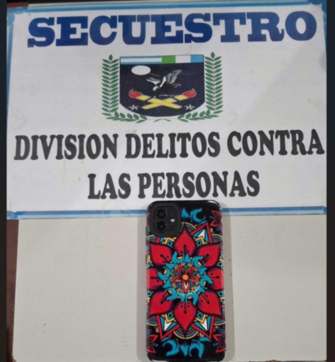 Un teléfono celular con funda estampada se exhibe frente a un cartel de la División Delitos contra las Personas en el contexto de una investigación por una muerte en Chaco (Policía de Chaco)
