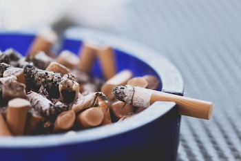 Cenicero azul con múltiples colillas de cigarrillos y cenizas. Una colilla, con filtro y tabaco quemado, descansa en el borde