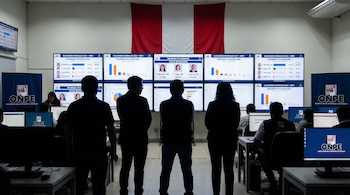 Múltiples pantallas con resultados de Elecciones Presidenciales Perú 2024 en centro de cómputo ONPE. Varias personas observan los datos. Bandera peruana al fondo.