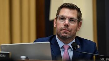 Un hombre caucásico de mediana edad, Eric Swalwell, con gafas y barba, lleva un traje azul y corbata rosa mientras mira hacia adelante