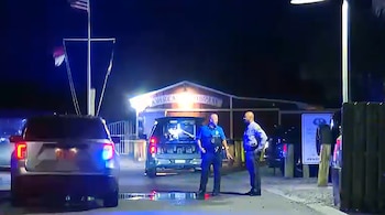 Dos agentes de policía conversan de noche en la calle frente a patrullas con luces encendidas y un edificio iluminado al fondo