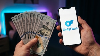 Manos con un abanico de billetes de cien dólares estadounidenses y un teléfono que muestra la aplicación de OnlyFans.