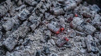Primer plano de brasas grises casi completamente cubiertas de ceniza, con algunos trozos de carbón aún mostrando un tenue color rojizo.